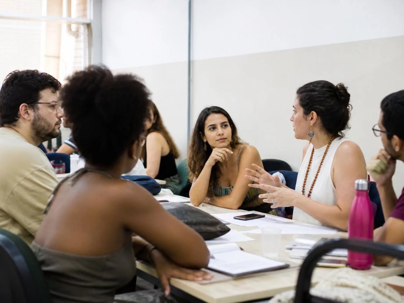 Participante com a mão erguida para pedir a palavra em uma mesa cheia de anotações